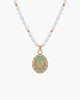 Macro view of a vintage gold butterfly relief pendant with a light green enamel base and zircon halo on a white pearl strand.