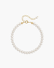 Top view of a delicate white pearl strand bracelet with gold lobster clasp and extension chain on a white porcelain dish.