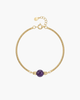 Close-up of a gold-plated snake bone chain bracelet featuring a central natural purple amethyst bead on a white background.