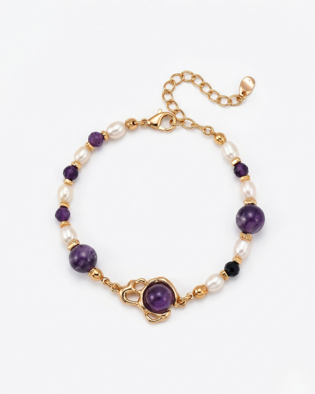 Overhead view of a natural amethyst and pearl beaded bracelet with a central golden planet-shaped charm on a white textured background.